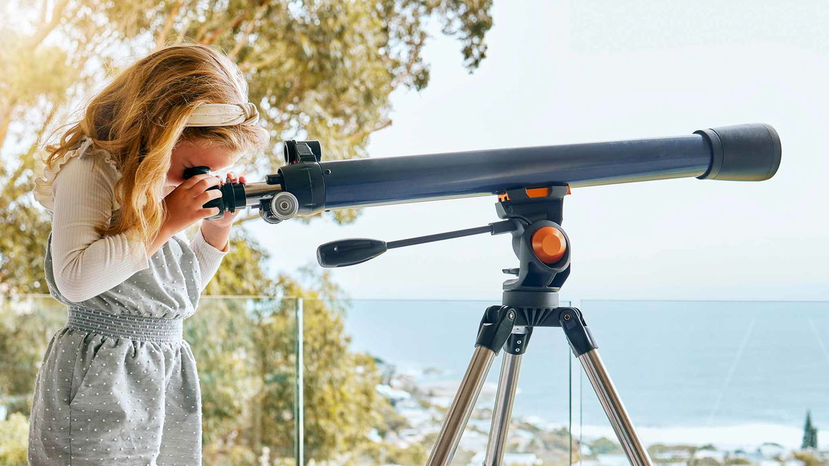 bambina che usa telescopio al mare