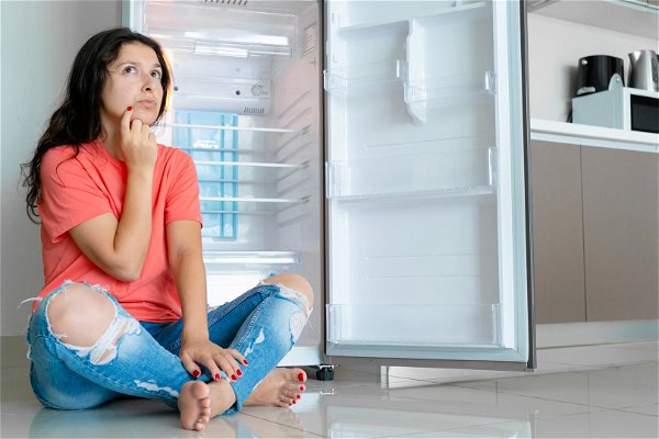 ragazza seduta davanti a frigorifero vuoto