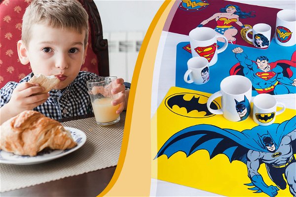 bimbo che mangia su una tovaglietta monocolore e tovagliette di batman, wonderwoman e superman sulla destra con grafica