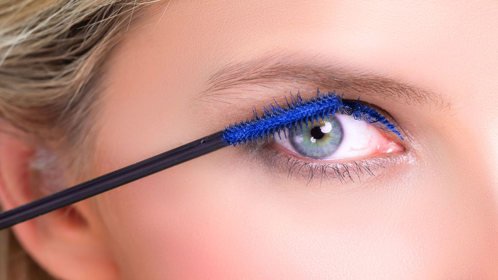 donna con occhi chiari che si mette mascara blu