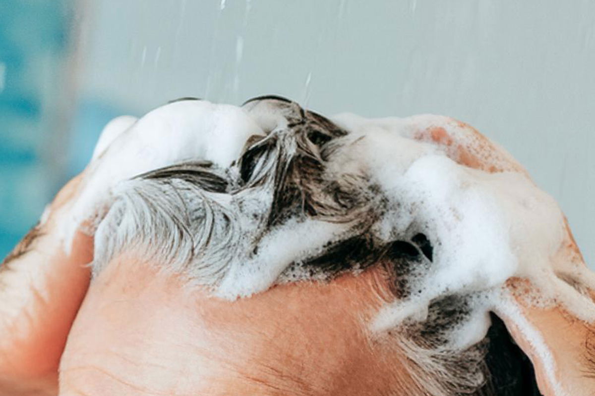 uomo con capelli bianchi che uso lo shampoo alpecin