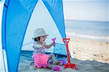 bimba che gioca sotto una tenda da sole in spiaggia