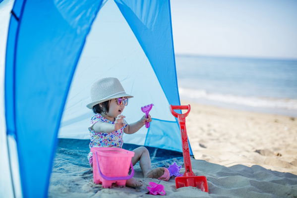 bimba che gioca sotto una tenda da sole in spiaggia