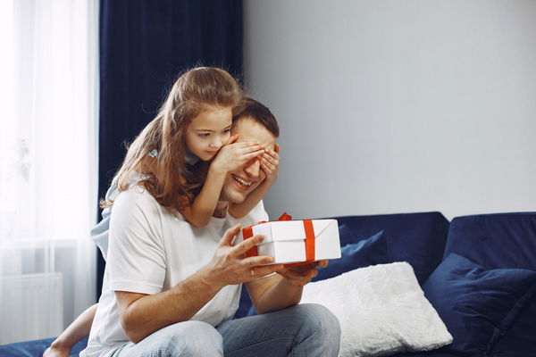 Bambina con le mani sugli occhi del papà che tiene un panchetto in mano